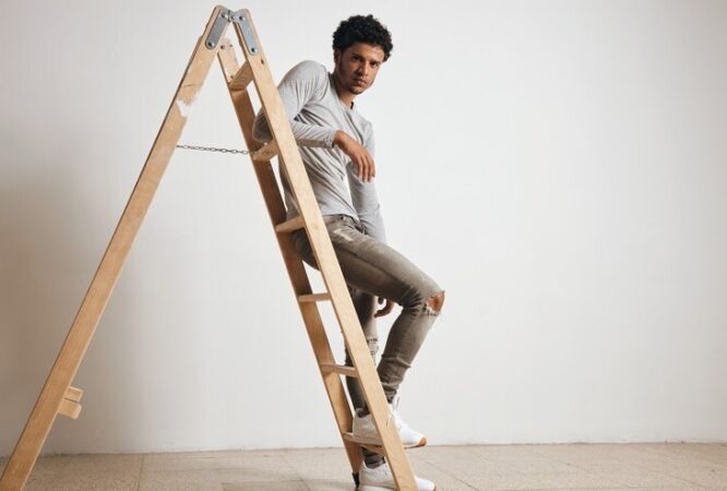 young-sexy-latin-guy-wears-blank-grey-henley-longsleeve-jeans-sits-wooden-ladder-isolated-white_346278-1037