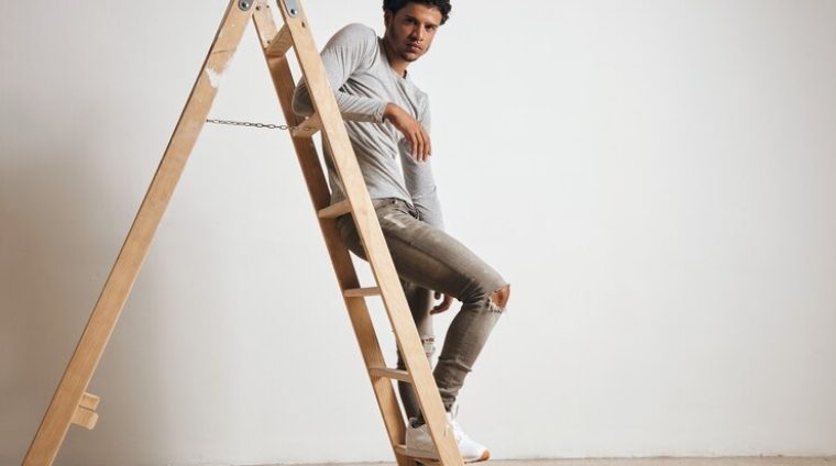 young-sexy-latin-guy-wears-blank-grey-henley-longsleeve-jeans-sits-wooden-ladder-isolated-white_346278-1037