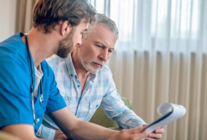 focused-serious-gray-haired-man-plaid-shirt-looking-clipboard-doctor-hands_259150-57378