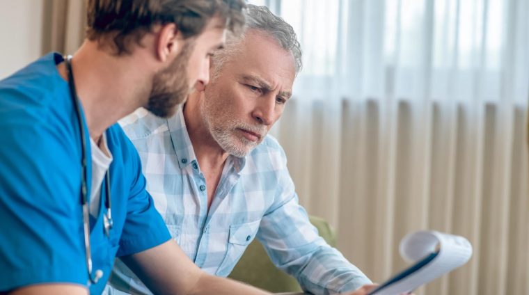 focused-serious-gray-haired-man-plaid-shirt-looking-clipboard-doctor-hands_259150-57378